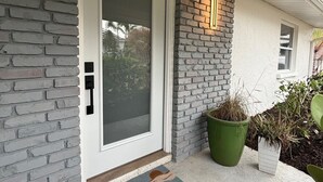 Ein modernes Haus mit Backsteinfassade, einer weißen Tür mit Glasfenster und einem grünen Blumentopf daneben.