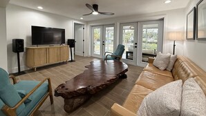 Ein modernes Wohnzimmer mit einem großen Holztisch, einer Ledersofa, einem Fernseher und einem Deckenventilator.