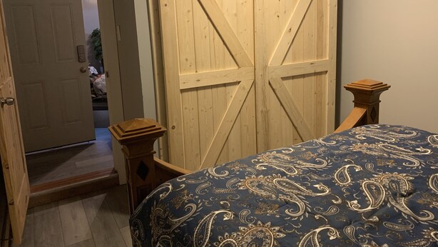 Ein Schlafzimmer mit großem Holzschrank, einem Bett mit gemustertem Überwurf und einem kleinen Nachttisch.