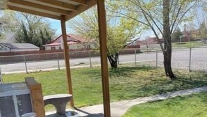 Ein überdachter Patio-Bereich mit Betonboden, einer Holzw pergola und einem Kübel mit Blumen, sowie einem Grill.