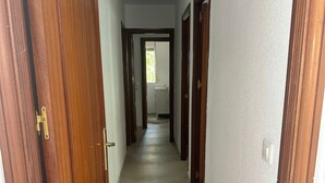 Corredor com portas de madeira e piso de azulejos, que leva a um banheiro com pia e janela.