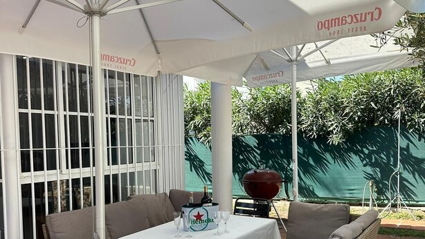 Uma área externa com mesas, cadeiras e um grande guarda-sol.