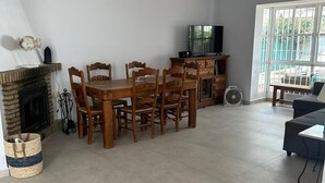Uma sala de jantar com mesa e cadeiras de madeira, televisão e lareira.