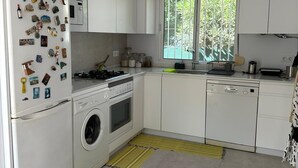 Uma cozinha moderna com armários brancos, forno embutido, máquina de lavar e janela com vista para o verde.