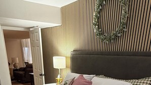 Un lit bien fait, avec une couette blanche, une tête de lit ornée de lattes de bois verticales et une guirlande décorative accrochée au mur.