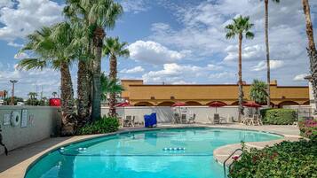 A swimming pool with lounge chairs and umbrellas, surrounded by palm trees and a building with arches in the background.