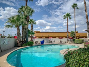 A swimming pool with lounge chairs and umbrellas, surrounded by palm trees and a building with arches in the background. - Studio 6 Laredo, TX - North I-35 (Laredo)