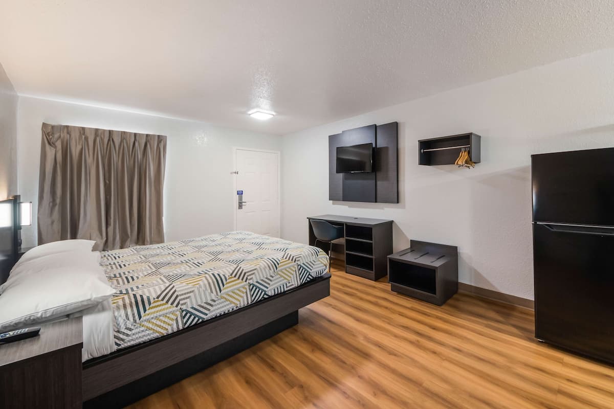 A modern hotel room with a bed, a desk, a TV, and a refrigerator.