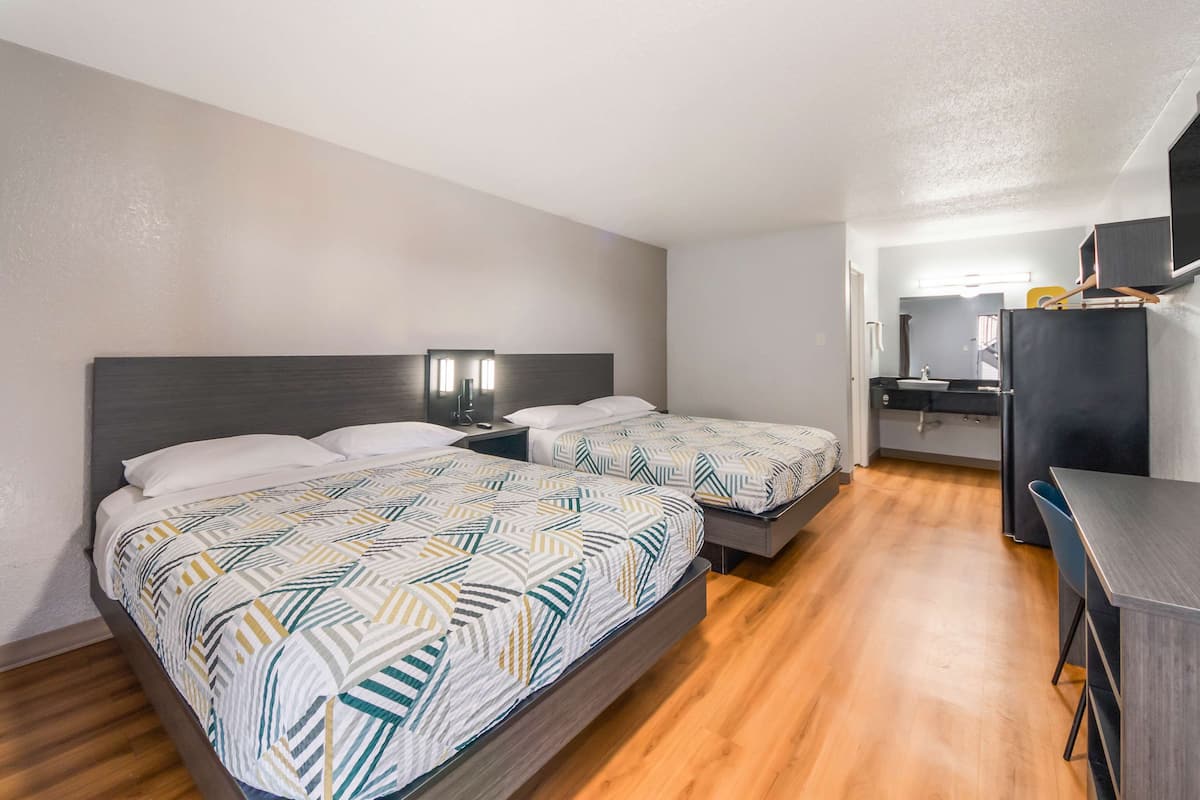 A hotel room with two beds, a desk, a mirror, and a TV.