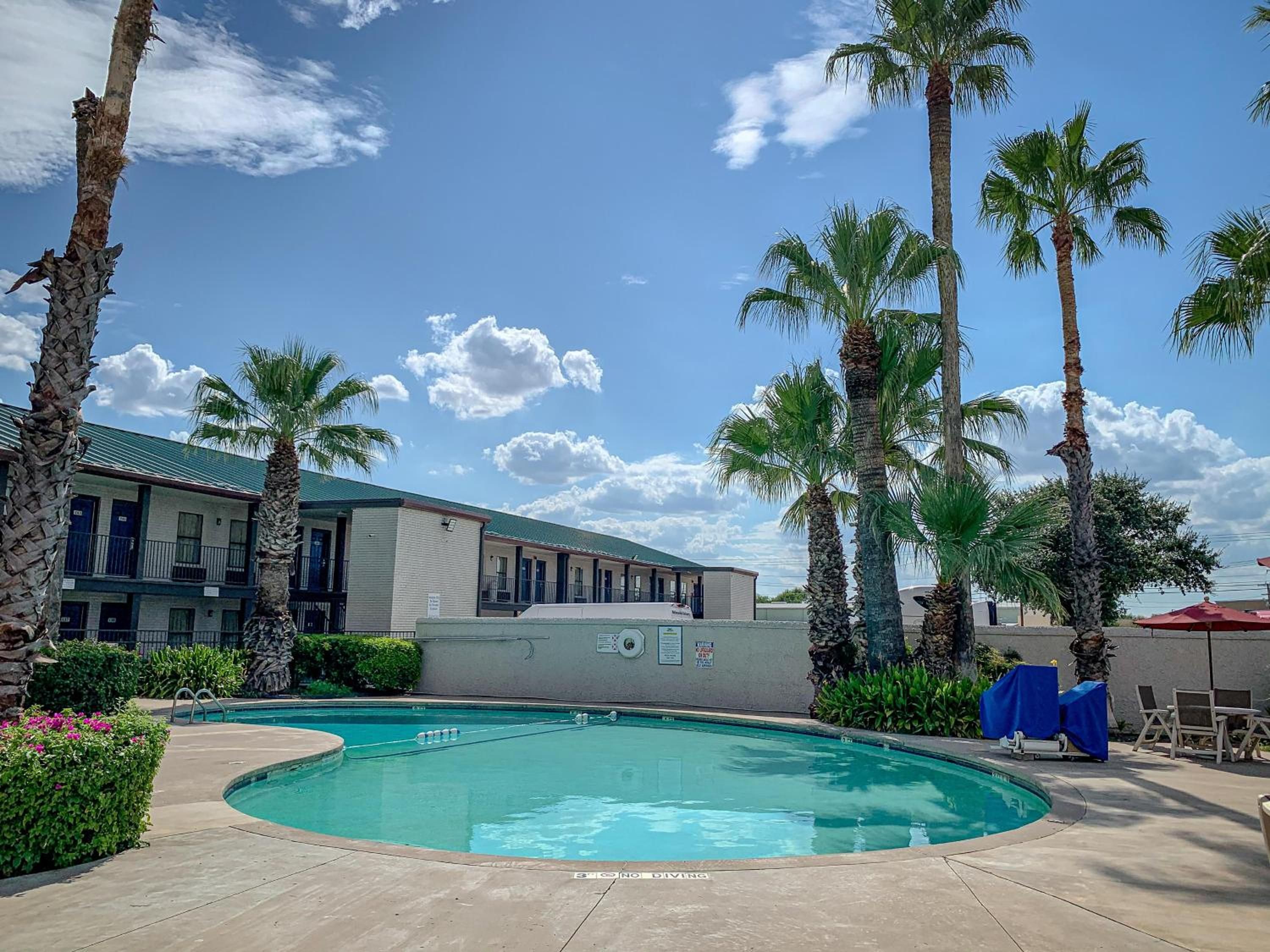 A pool area with a clear sky, palm trees, and a building with a green roof.