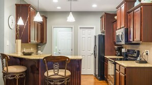 A kitchen with wooden cabinets, a central island with bar stools, a refrigerator, and a microwave. - Branson Townhome Near Hwy 76 | Pool | Garage | Sleeps 8 (Branson)