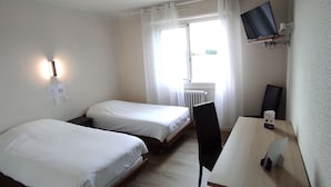 Habitación de hotel con dos camas individuales, un escritorio con silla, televisor montado en la pared y una ventana con cortinas.