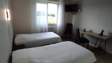 Habitación de hotel con dos camas individuales, un escritorio con silla, un televisor montado en la pared y una ventana con cortinas.
