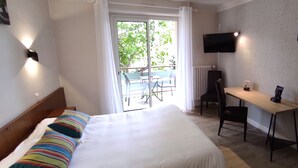 Habitación de hotel con cama, escritorio, silla, televisor y balcón con vistas a árboles.