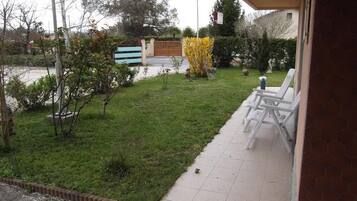 Un patio con suelo de baldosas, una pequeña zona de césped y algunas sillas.