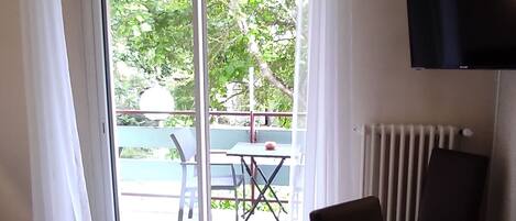 A hotel room with a bed, a desk, a chair, a TV, and a sliding glass door leading to an outdoor area with a table and chairs.