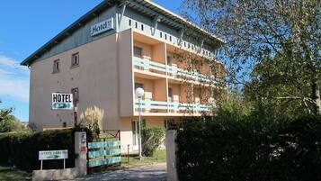 Un hotel de dos pisos con un balcón en el piso superior, un cartel que indica la entrada de estacionamiento y un cielo despejado.