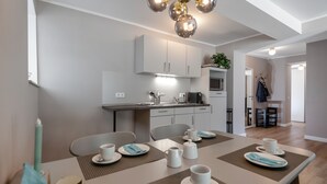 Een moderne eetruimte met een keuken op de achtergrond, een gedekte eettafel met borden, bekers en bestek, en een kroonluchter erboven.