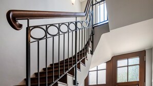 Een trap met een houten leuning en metalen spijbels, die leidt naar een kamer met vloertegels met een patroon en een houten deur.
