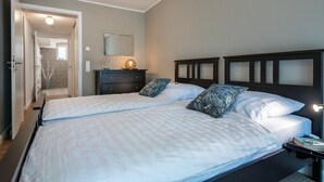 Een slaapkamer met twee bedden, een dressoir, een spiegel en een nachtkastje met een lamp.