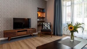 Een moderne woonkamer met een flatscreen televisie, een houten tv-meubel, een comfortabele fauteuil, een salontafel en een vaas met zonnebloemen.