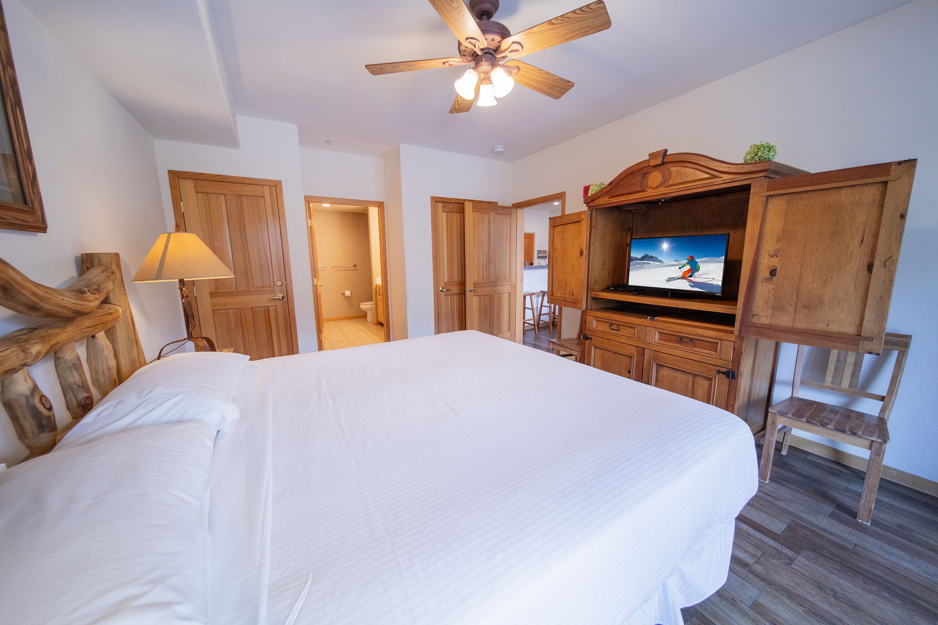 Un dormitorio con una cama grande, cabecera de madera, ventilador de techo, televisor y un mueble de madera.
