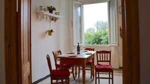 Ein Essbereich mit Tisch für vier Personen, Holzstühlen, einer Pendelleuchte und einem Fenster mit Blick auf Grünfläche.