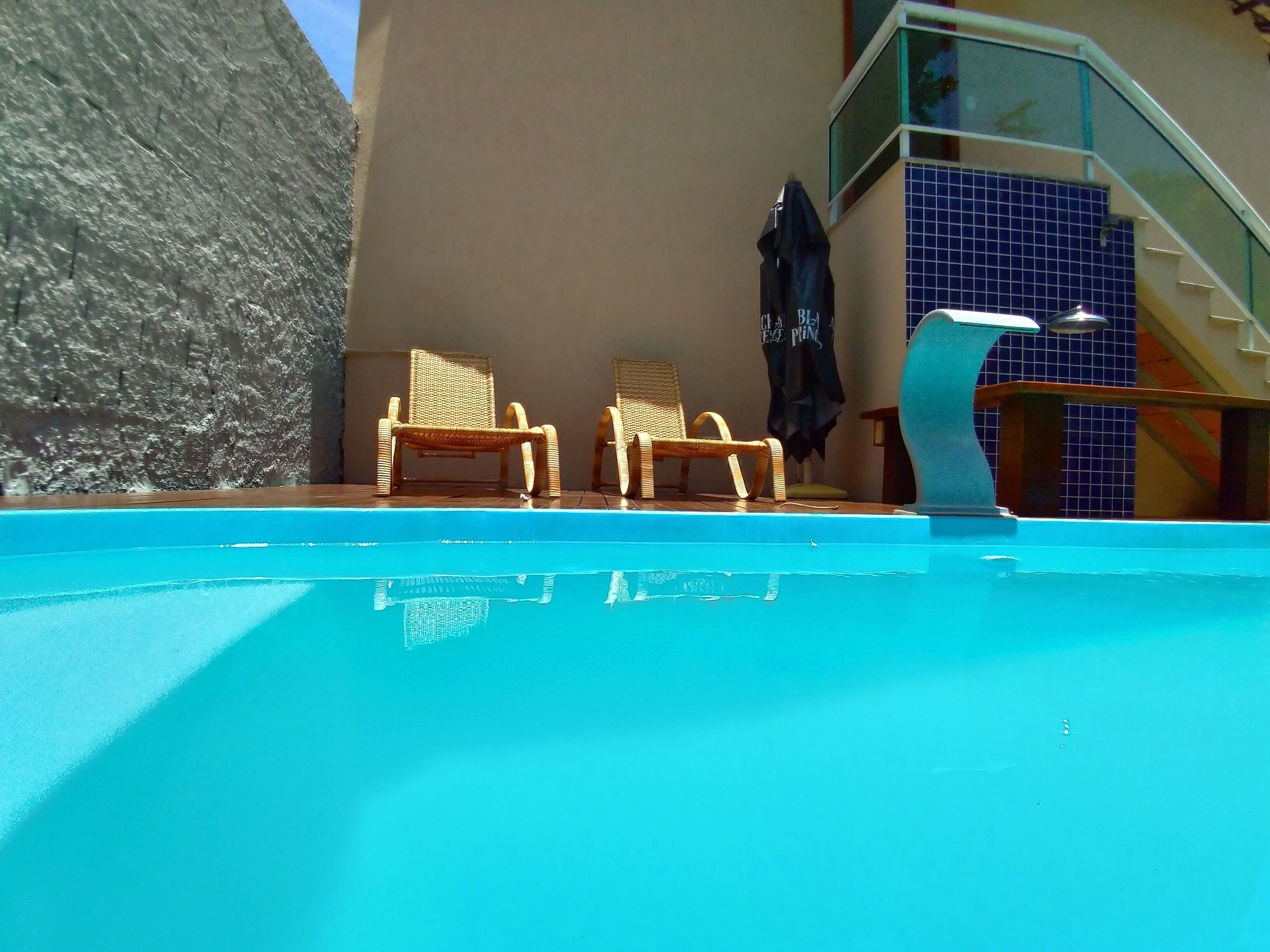 Piscina com duas cadeiras de vime e área coberta.