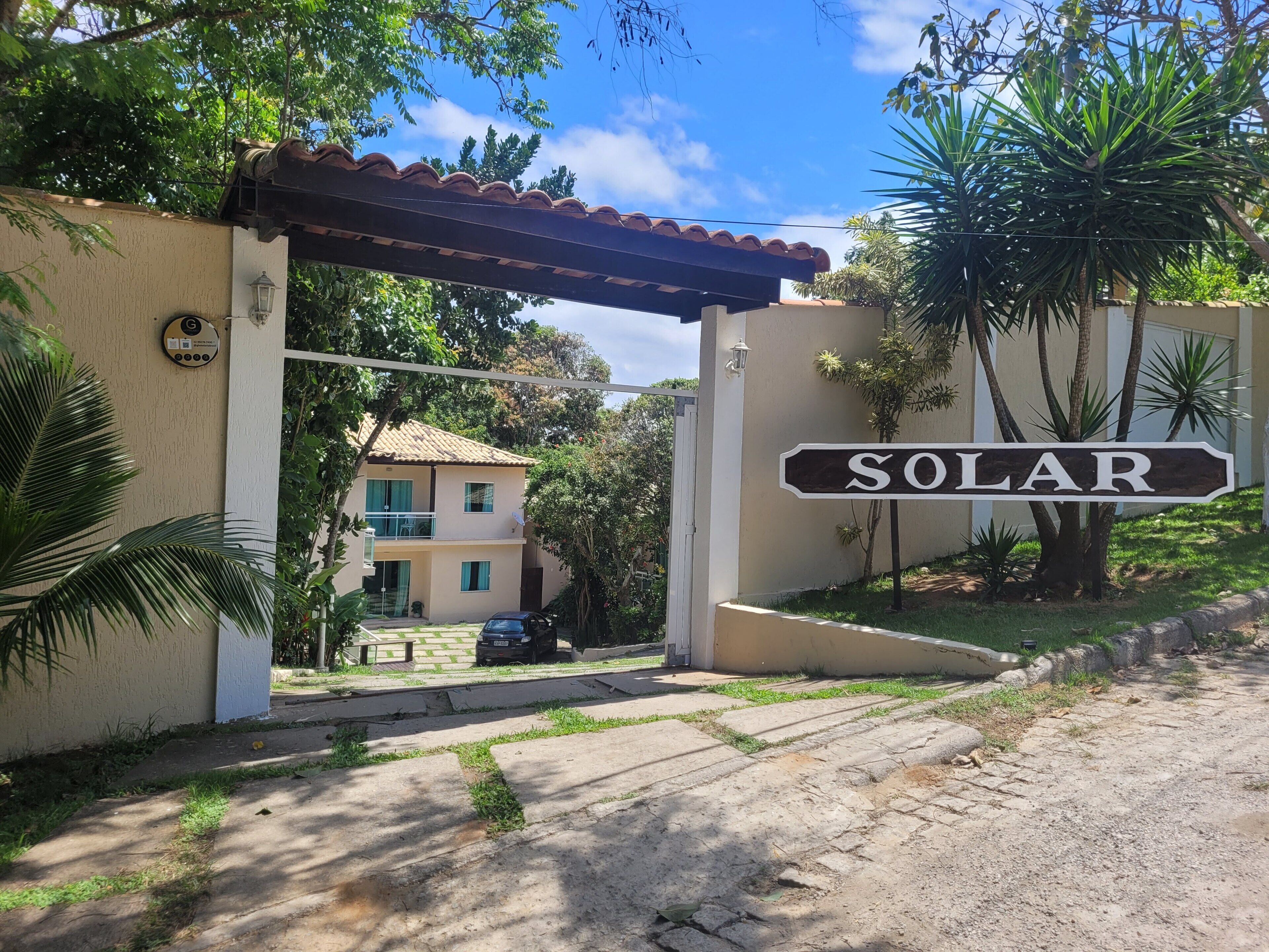 A gated entrance with a 'SOLAR' sign, a two-story building with a tiled roof, and a car parked in front.