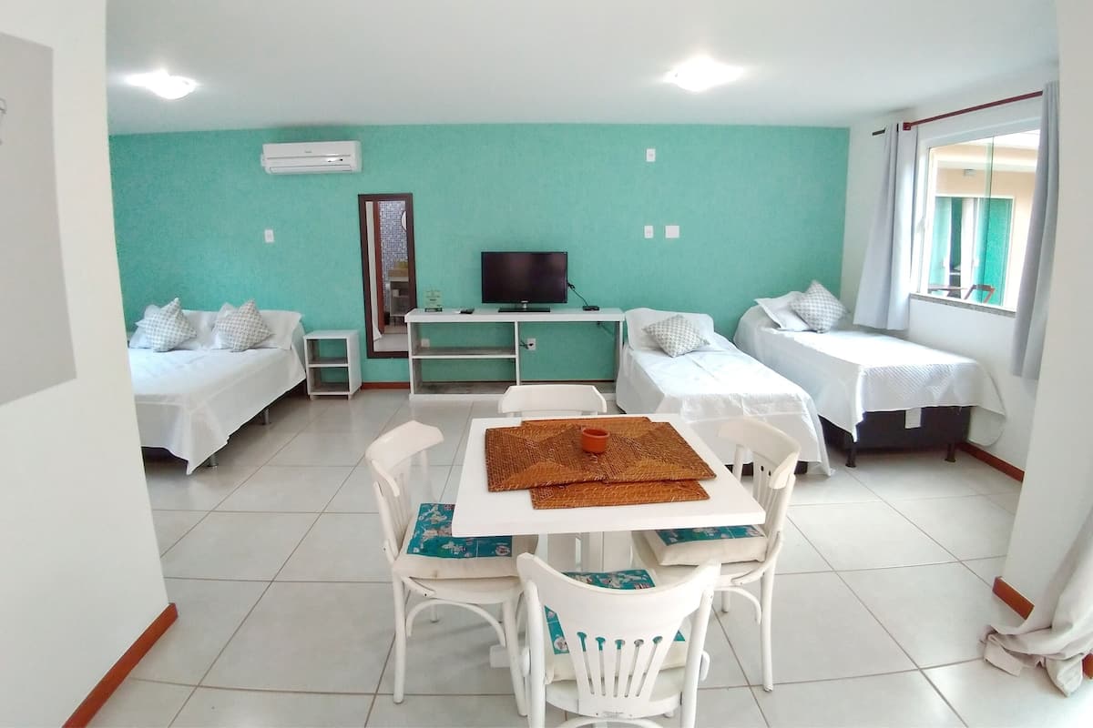 Una habitación con dos camas, un escritorio con televisor, una mesa de comedor con sillas y una ventana con cortinas.