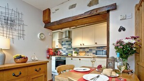 Une cuisine avec des meubles de rangement en bois, une table à manger avec des chaises, une horloge et un vase rempli de fleurs.