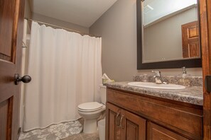 A bathroom with a shower curtain, toilet, sink, and mirror.
