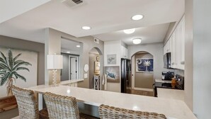 A modern kitchen with a central island, wicker chairs, and a refrigerator.