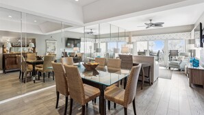 A spacious dining area with a glass table and wicker chairs, a kitchen with a TV, and a balcony with a view.