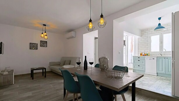 Uma sala de estar moderna com sofá, mesa de jantar e cadeiras. Há uma área de cozinha com armários e uma janela.