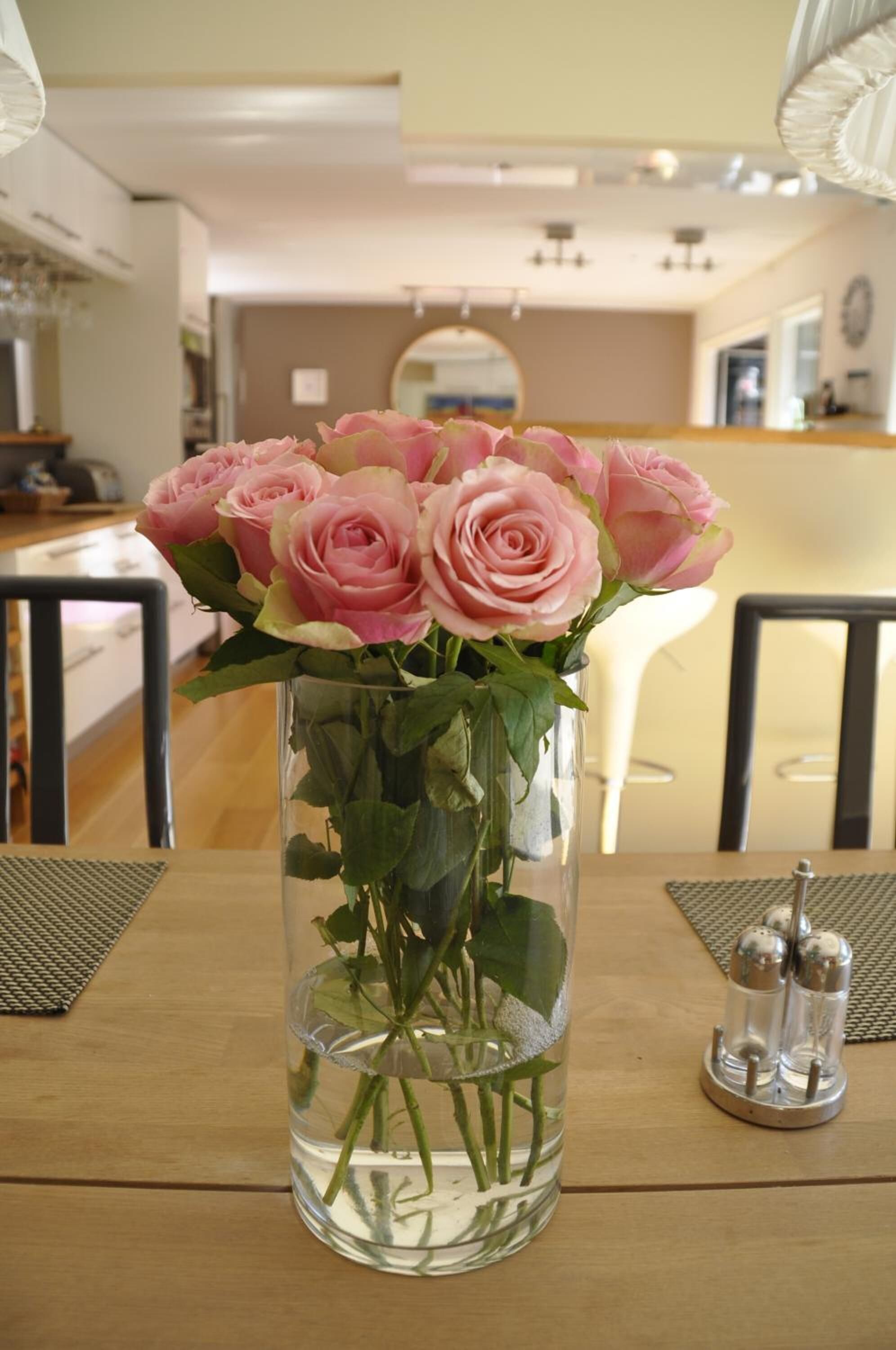 Un vase en verre transparent contenant des roses roses, posé sur une table en bois.