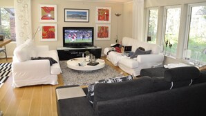 Una sala de estar con dos sofás blancos, un sofá negro, una mesa de centro y un televisor.