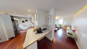 A modern kitchen with a microwave, toaster, and coffee maker, a dining area with a table and chairs, and a living room with a sofa and a plant. - quai koch 90m2 city center    3br (Strasbourg)