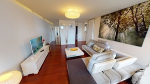 A modern living room with a flat-screen TV, a sofa, a coffee table, and a painting on the wall. - quai koch 90m2 city center    3br (Strasbourg)