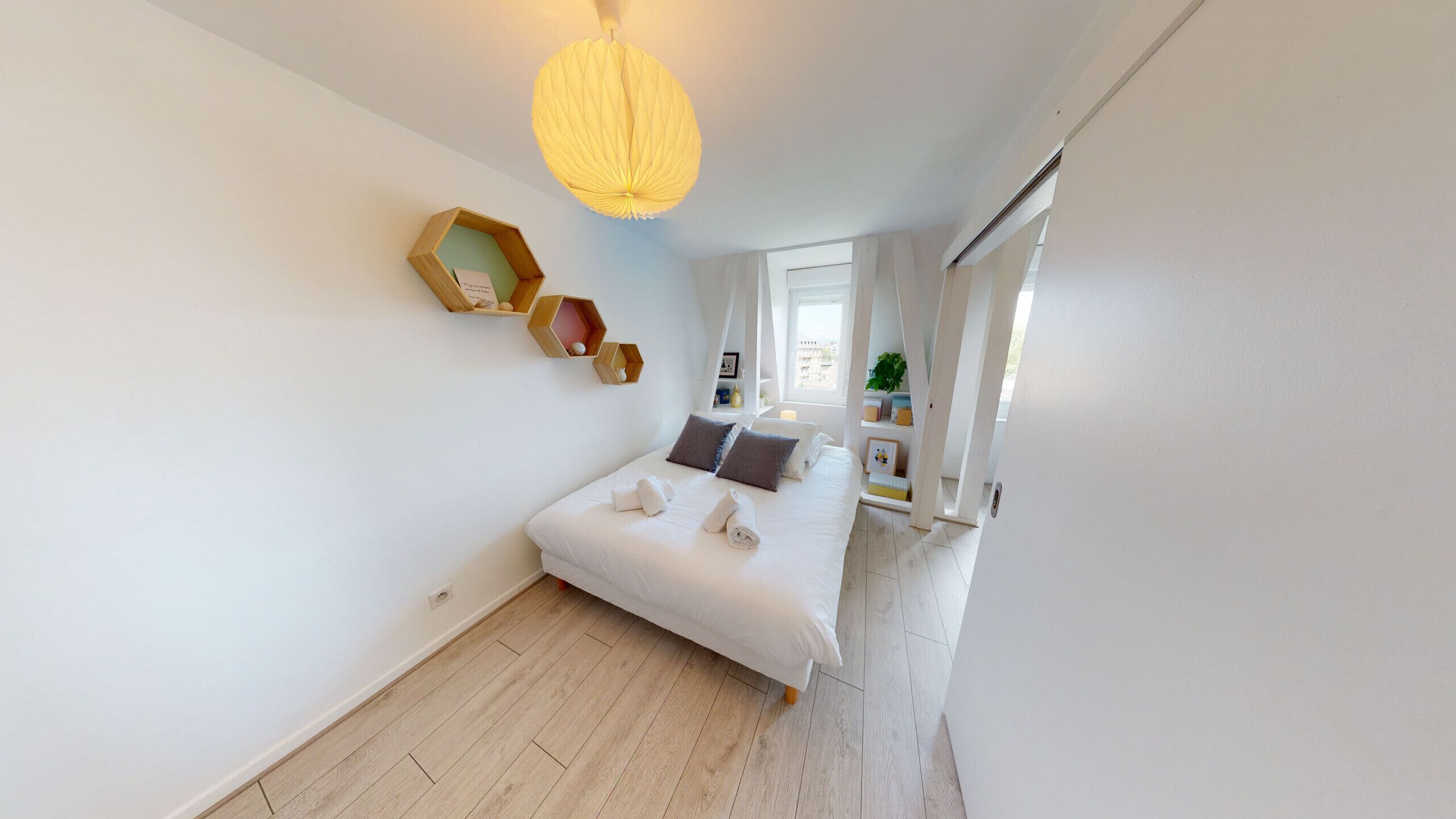 Een slaapkamer met een bed, een houten plank, een hanglamp en een raam.