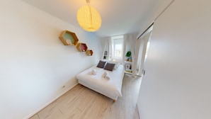 A bedroom with a bed, a wooden shelf, a hanging light fixture, and a window. - quai koch 90m2 city center    3br (Strasbourg)