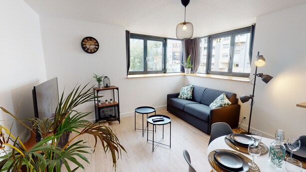 A modern living room with a sofa, a coffee table, a TV, a bookshelf, and a dining area with a table set for two.