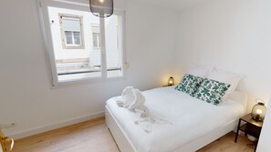 A bedroom with a bed, a window, a nightstand with a lamp, and a towel on the bed.