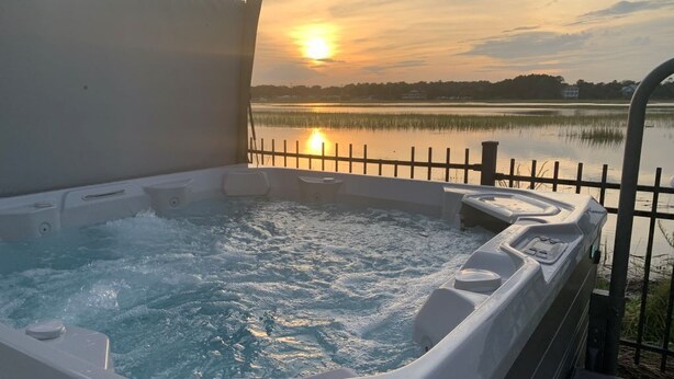 Ett bubbelbad med utsikt över en solnedgång över en sjö.