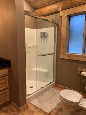A glass-enclosed shower with a wooden ceiling, a toilet, and a window above the sink. - Aspen Cabin (Packwood)