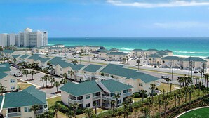 A coastal hotel with multiple-story buildings, a parking lot, and a view of the ocean.