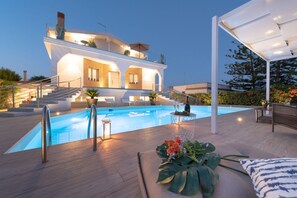 Eine moderne Villa mit Schwimmbad, Sitzgelegenheiten im Freien und einer überdachten Terrasse.