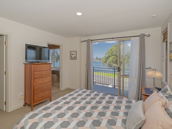 A bedroom with a bed, a dresser, a TV, and a balcony with a view of the water. - Tairua Waterfront Retreat - Tairua Apartment (Tairua)