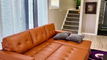 A living room with a brown leather sofa, a purple rug, and a staircase leading to a second floor.