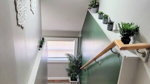 Un escalier avec des marches en bois, une rampe et une étagère fixée au mur, ornée de plantes.